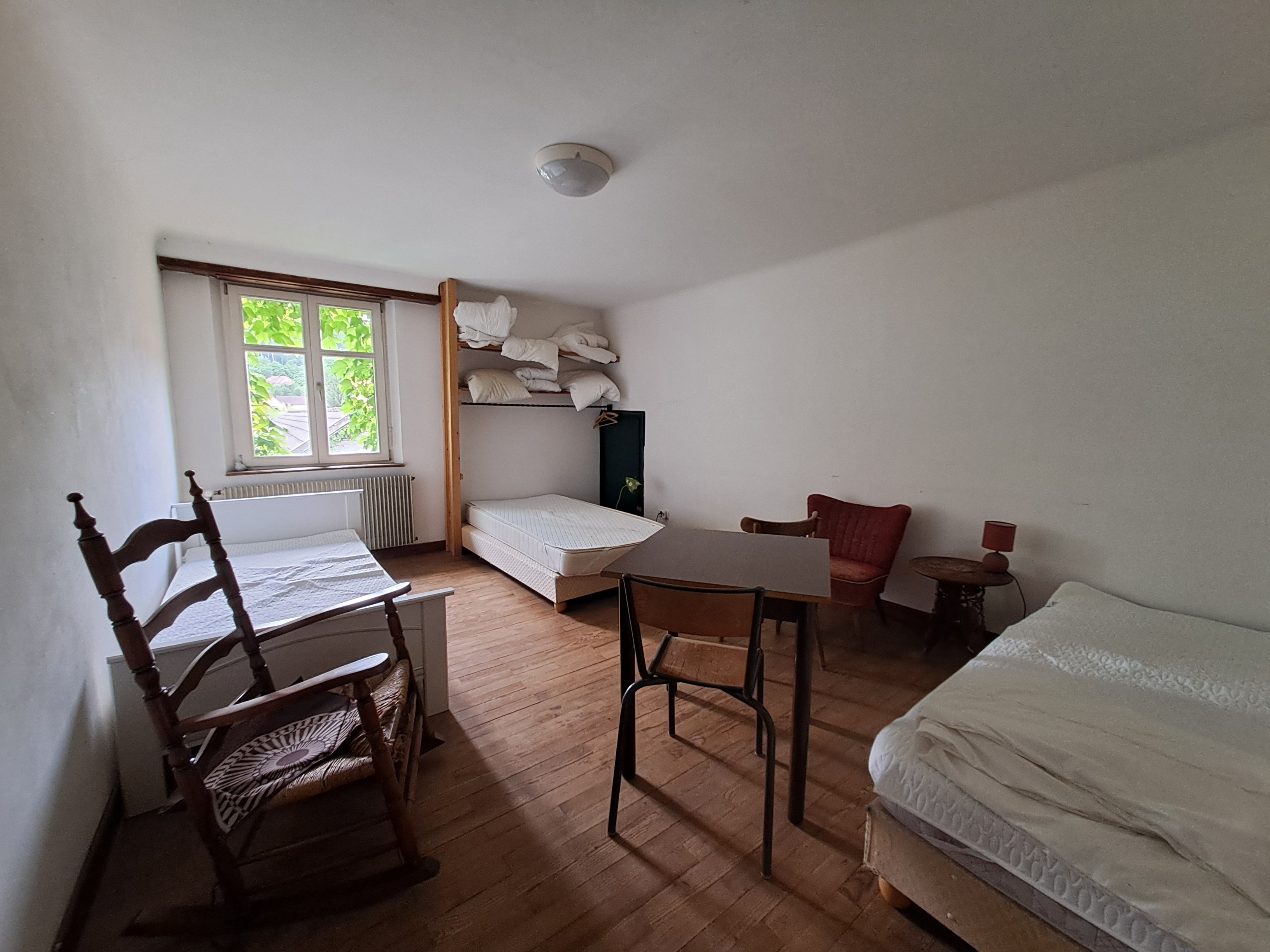 une dortoit composé de trois lits avec une table une chaise deux fauteuils du parquet et une fenêtre